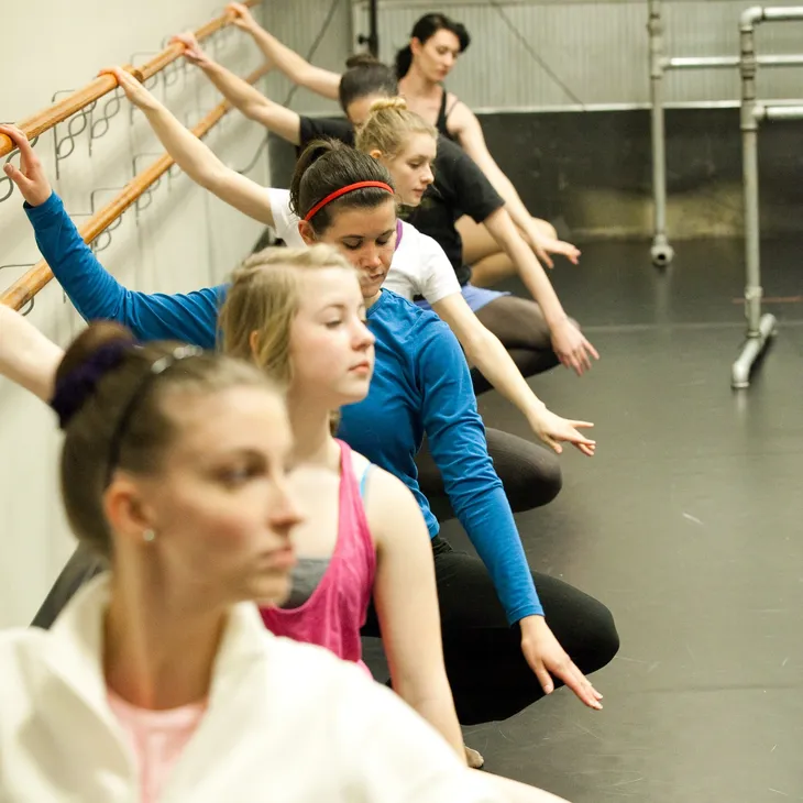 a group of adult ballet students stretching at the barre